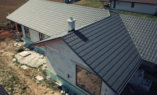 Střecha novostavby s šedými taškami na pozadí nezpevněného terénu.