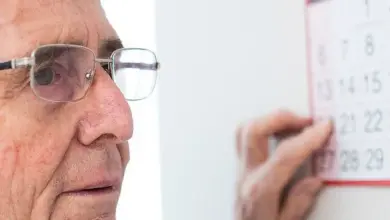 Starší muž s brýlemi se dívá na kalendář a ukazuje prstem datum.