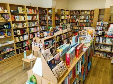 Vnitřek knihkupectví s dřevěnými regály plnými barevných knižních titulů.