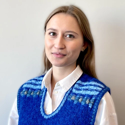 Žena v modrém svetrku s bílou košilí na neutrálním pozadí.