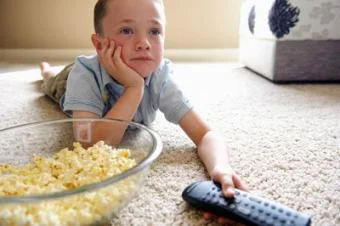 Chlapec leží na podlaze s misky popcornu v ruce.