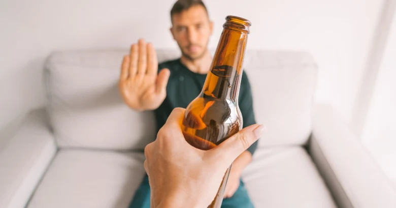 Ruka drží pivo, zatímco muž v pozadí gestem odmítá.