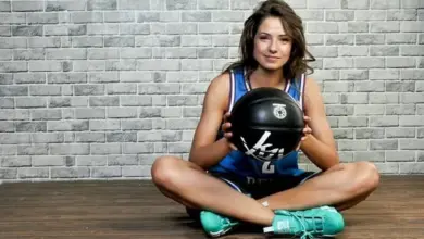 Dívka v dresu drží basketbalový míč před cihlovou zdí.