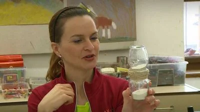Žena drží sluneční hodiny vyrobené ze dvou sklenic s pískem.