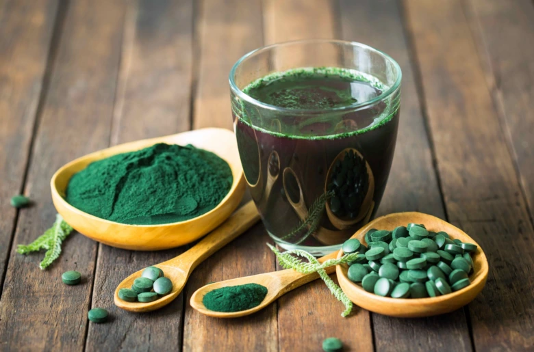 Sklenice s tekutou spirulinou vedle prášku a tablet.