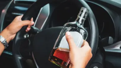 Ruce za volantem auta s lahví alkoholu v ruce.