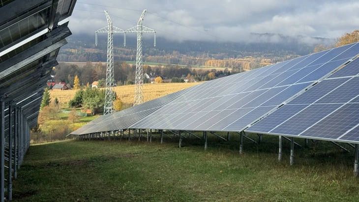 Fotovoltaické panely na svahu v krajinném prostředí s výhledem do údolí.