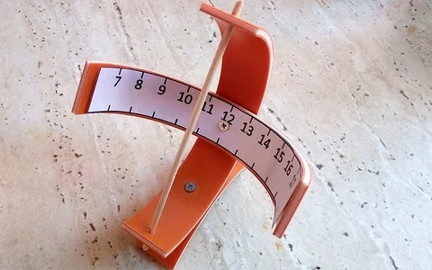 Domácí sluneční hodiny s oranžovým ciferníkem na kamenné podlaze.