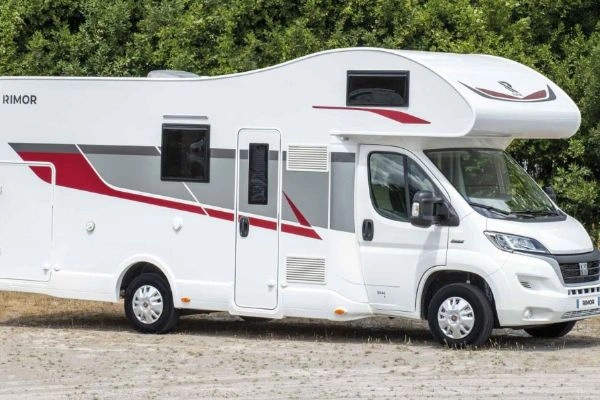 Bílý obytný vůz typu karavan zaparkovaný na štěrku.