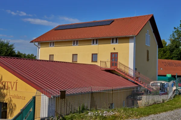 Žlutý dům s červenou střechou a solárními panely.