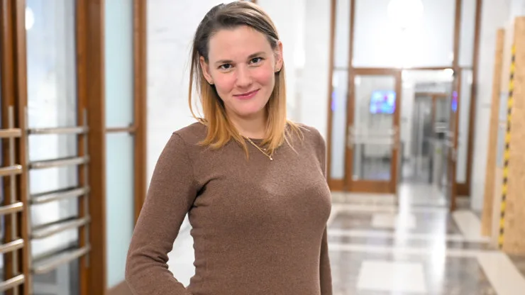 Portrét ženy v hnědém tričku stojící ve chodbě.