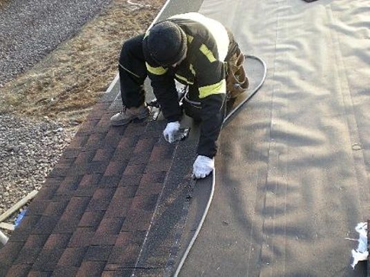 Stavebník montuje asfaltové šindele na plochou střechu.