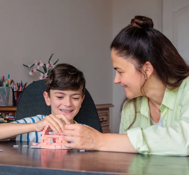 Žena s chlapcem staví geometrické tvary z barevných dílků.