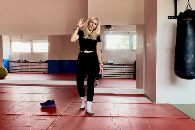 Žena v posilovně mává rukou s úsměvem.