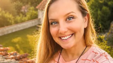 Usměvavá žena v růžovém tričku na venkovní pozadí.