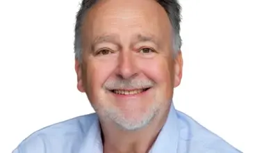 Portrét usměvavého muže s šedými vlasy v modré košili.