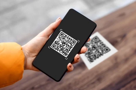 Ruka drží telefon s čtečkou QR kódu pro online podání daňového přiznání.
