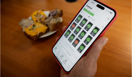 Ruka drží telefon s aplikací pro sledování stravy nad zdravou jídelníčkem.