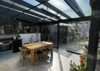 Moderní dřevěná pergola s plexisklovou střechou v zahradním prostoru.