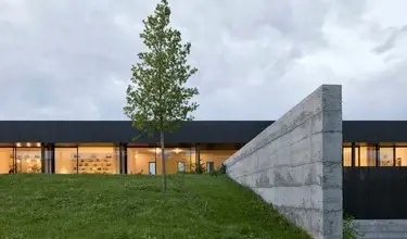 Moderní budova s travnatým svahem před ní pod šedou oblohou.
