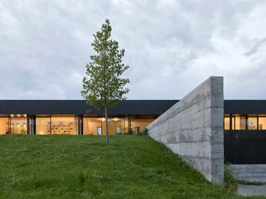 Moderní budova s travnatým svahem před ní pod šedou oblohou.