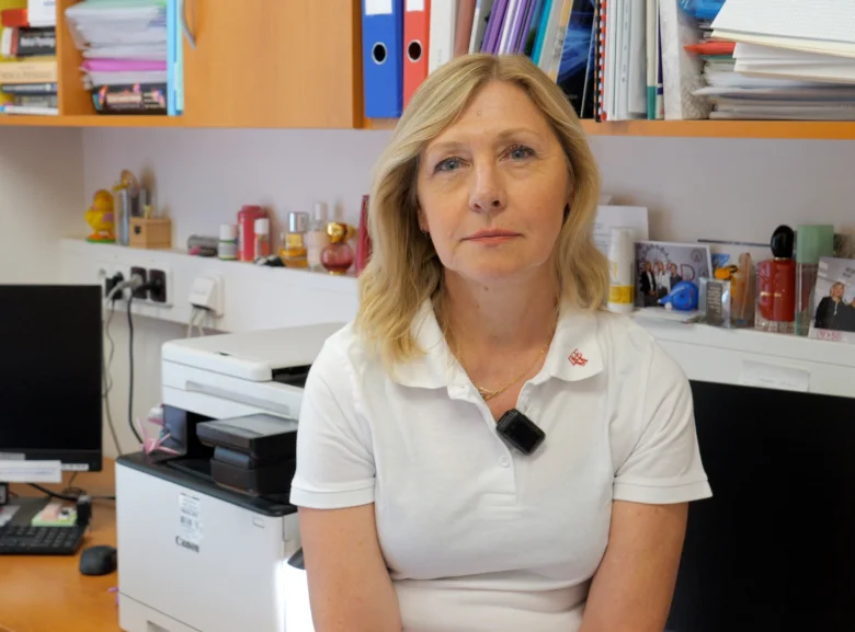 Žena sedí v kanceláři před tiskárnou s dokumenty na polici.