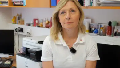 Žena v kanceláři s dokumenty na polici za ní.