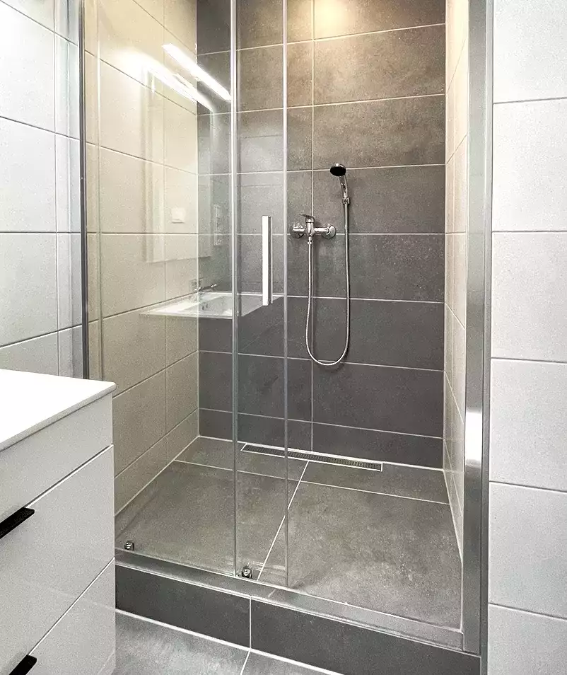 Moderní koupelna po rekonstrukci s sprchovým koutem a šedými dlaždicemi.