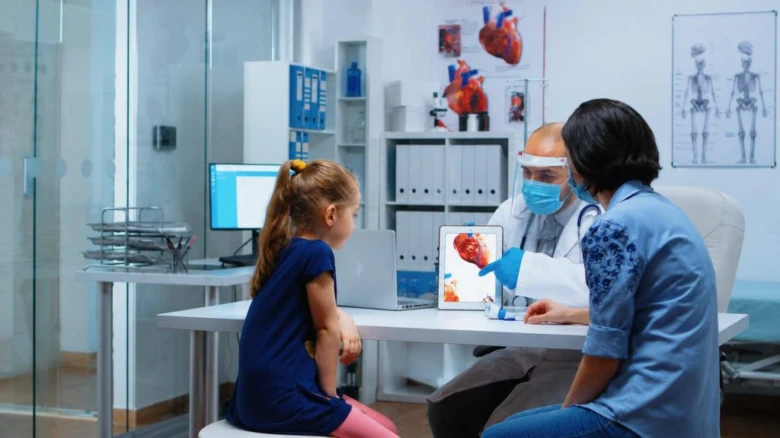 Lékař ukazuje dítěti digitální snímek srdce na tabletu v telemedicínském vyšetření.