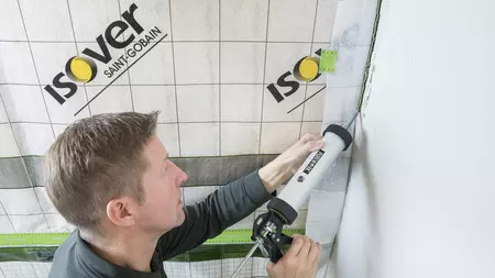 Muž těsní stěnovou izolaci pro regulaci vlhkosti v domácnosti.