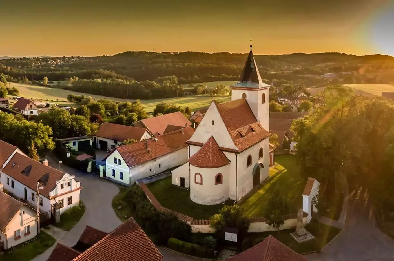 Kostel v vesnici při západu slunce s okolními domy.