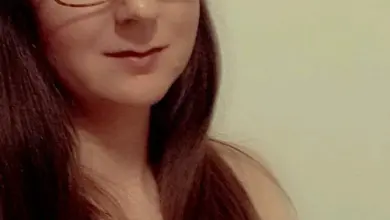 Žena s brýlemi se dívá na čtenáře v neutrálním prostředí.