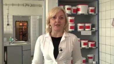 Žena v bílé lékařské pláši stojí ve zdravotnickém prostředí.