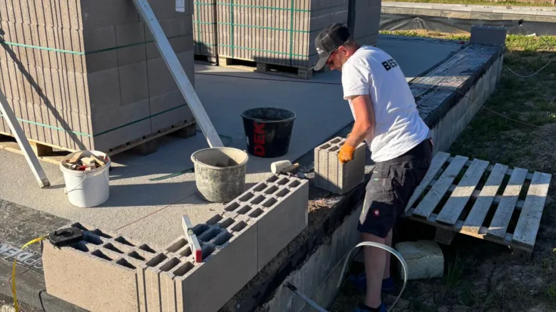 Muž kladí betonové bloky na zdi venku.