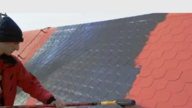 Muž aplikuje tekutou hydroizolaci na šindelovou střechu válečkem.