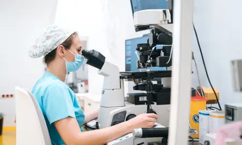 Vědkyně zkoumá buňky pod mikroskopem v laboratoři.