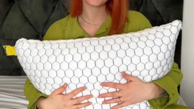 Žena v zeleném oblečení sedí na posteli s polštářem.