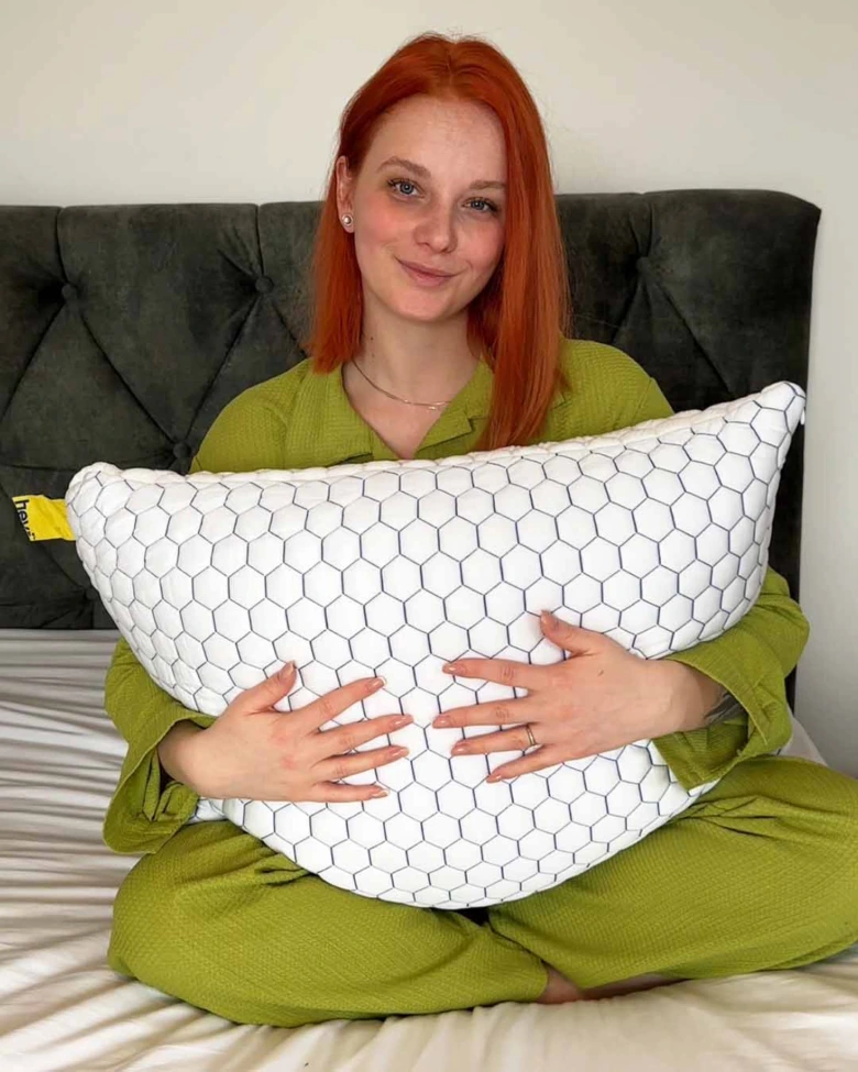 Žena v zeleném oblečení sedí na posteli s polštářem.