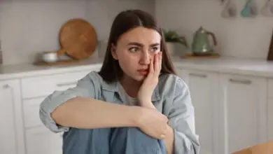 Žena sedí v kuchyni s výrazem úzkosti na obličeji.