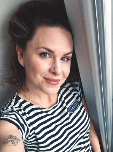 Žena v pruhované tričku se usmívá u okna.