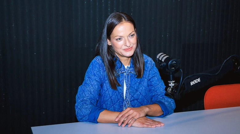 Žena sedí za stolem s mikrofonem v rozhovoru.