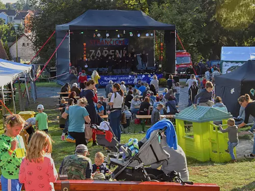 Venkovní festival s divadlem na scéně uprostřed trávníku.