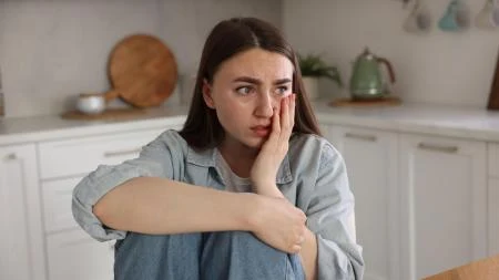 Dívka sedí v kuchyni s výrazem bolesti nebo úzkosti.