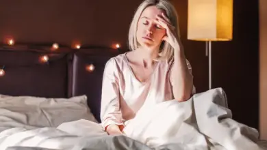 Žena sedí v posteli s bolestmi hlavy.