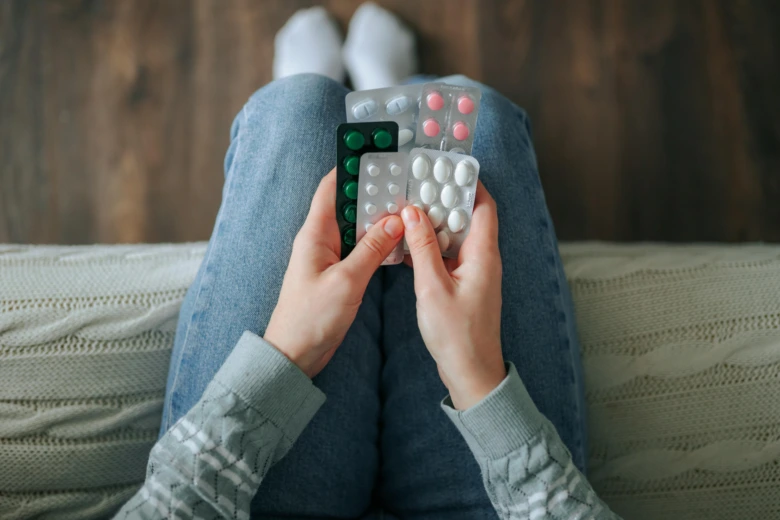 Osoba drží v klíně balíčky různých barevných tablet.