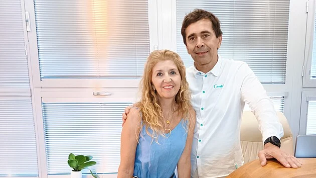 Muž a žena stojí v kanceláři, usmívají se na kameru.