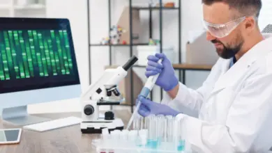 Vědec v laboratoři s mikroskopem, zkumavkami a počítačem.
