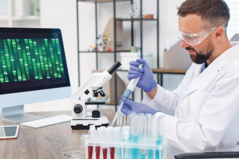 Vědec v laboratoři s mikroskopem, zkumavkami a počítačem.