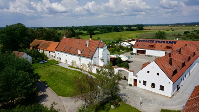 Bílá farma s červenými střechami na pozadí zelených polí.